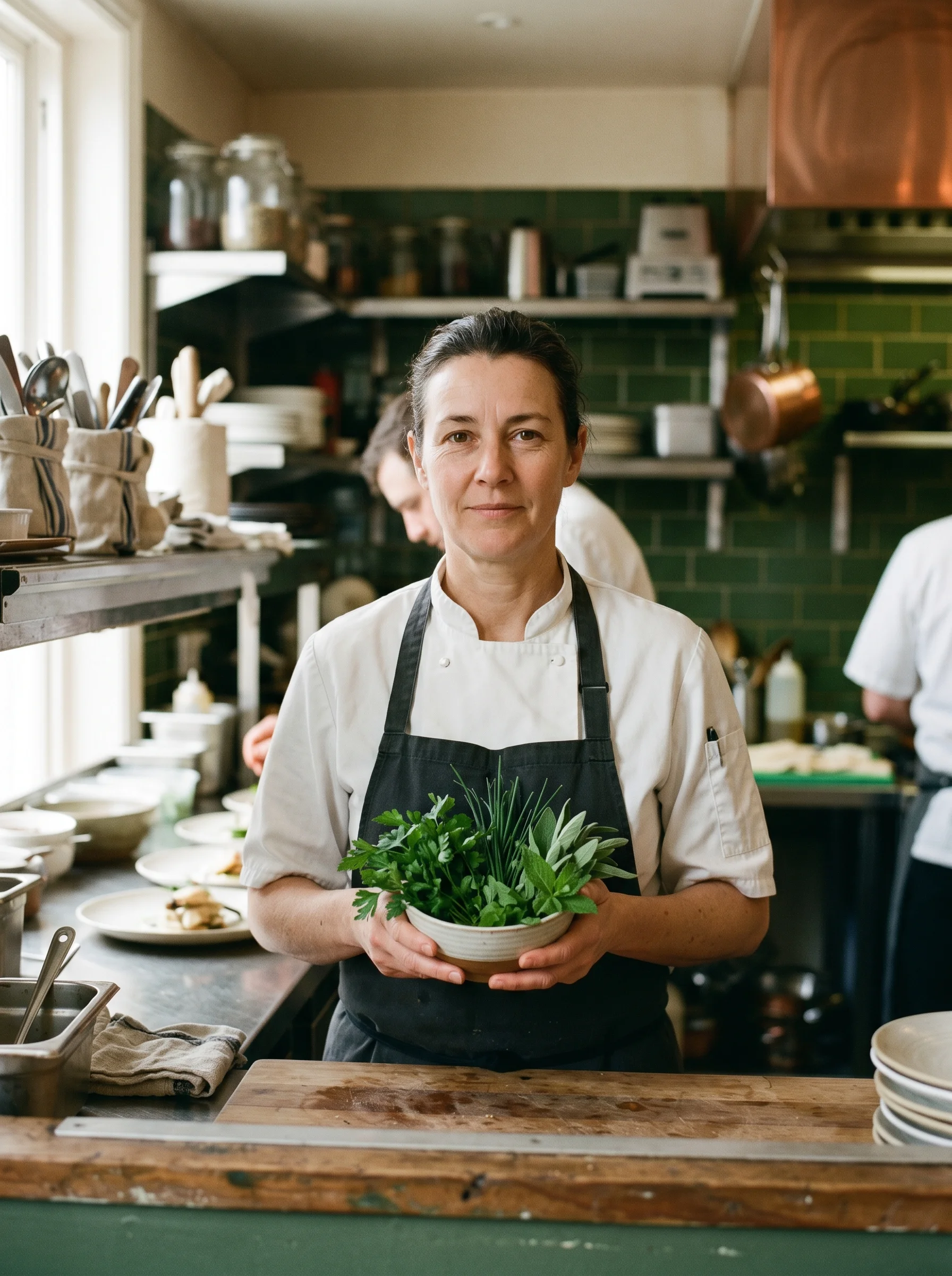 Chef-owner Mara Whitfield in her whites at the pass of The Copper Larder, holding fresh herbs